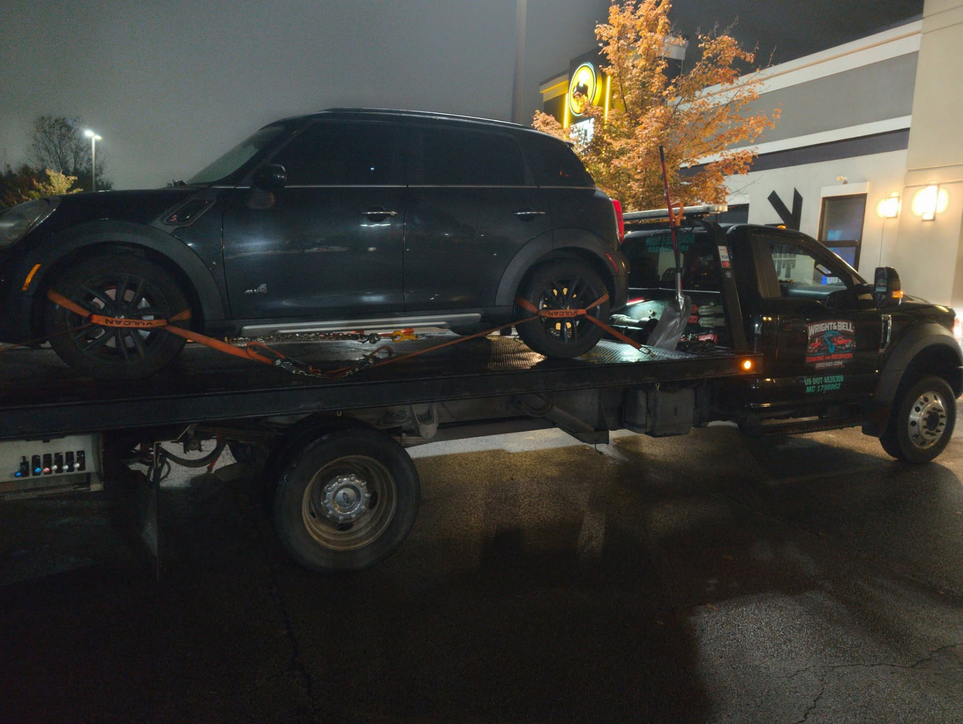An SUV secured on a flatbed tow truck at night