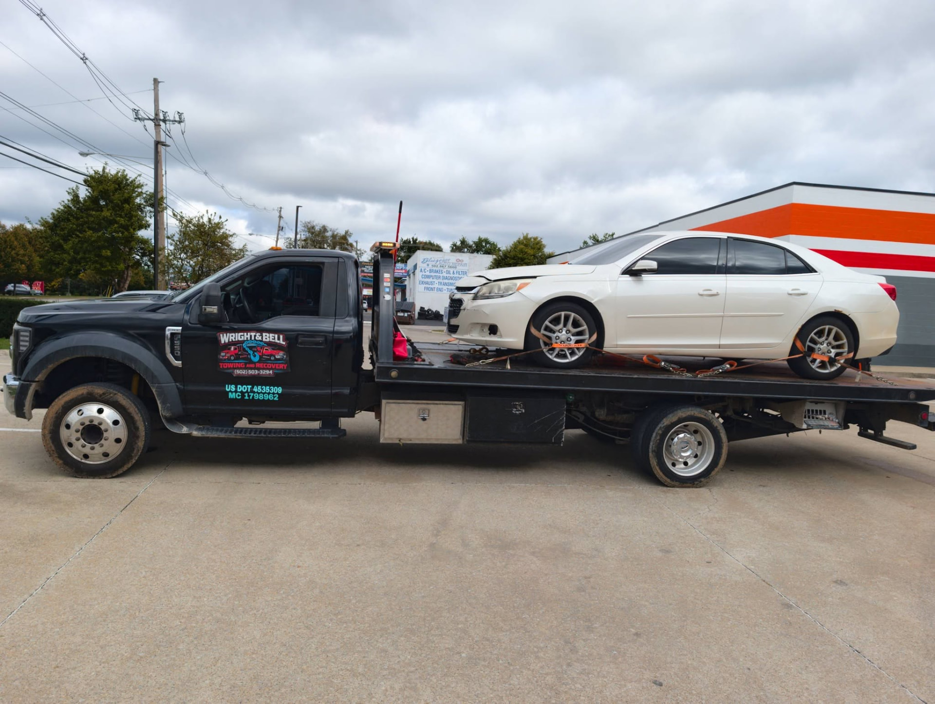 Wright & Bell flatbed tow truck carrying a white sedan